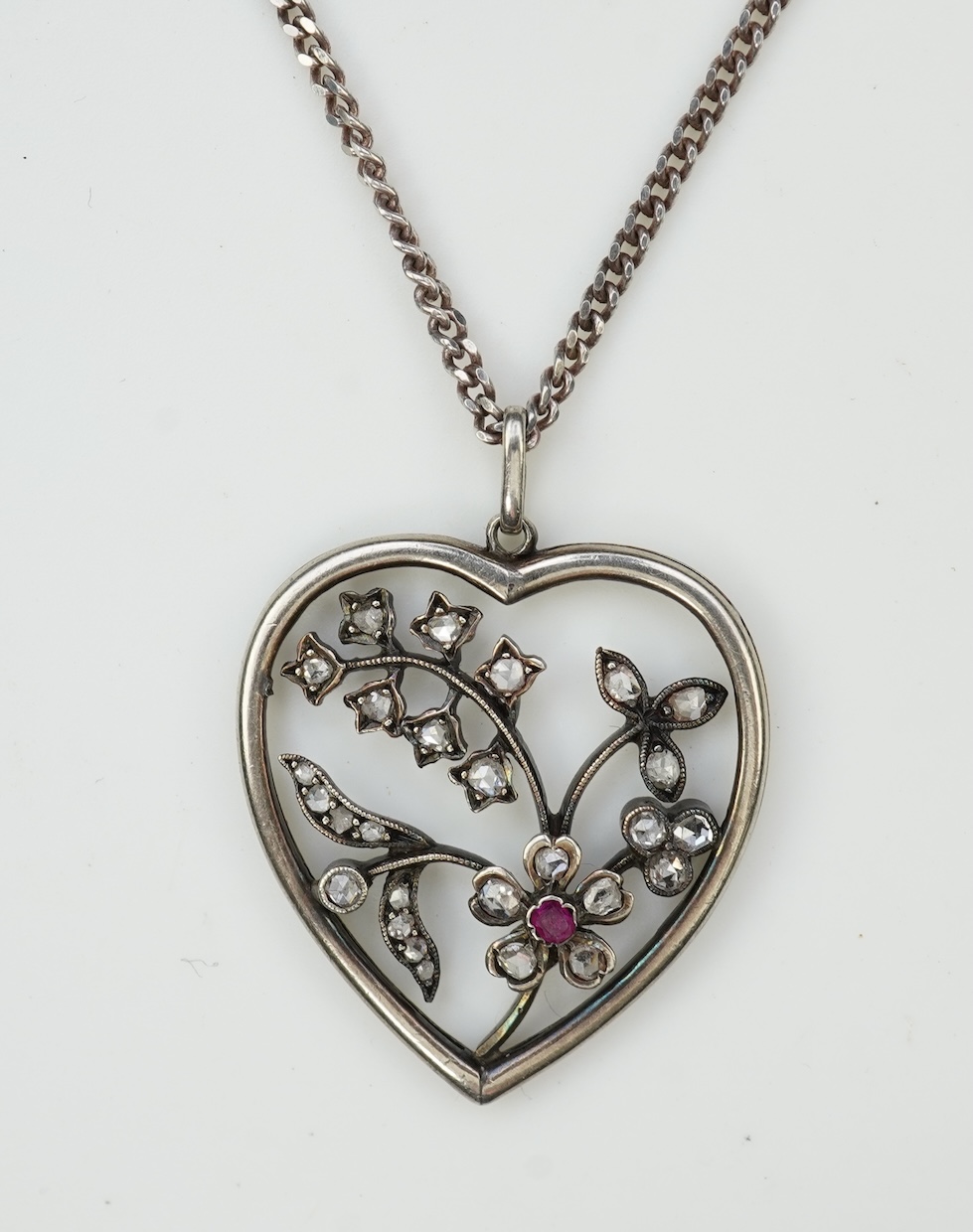 A diamond pendant, designed as a spray of flowers in a heart-shaped frame, set with rose-cut diamonds and a circular-cut ruby, to a later silver chain, pendant 3.1cm, chain length 44cm
